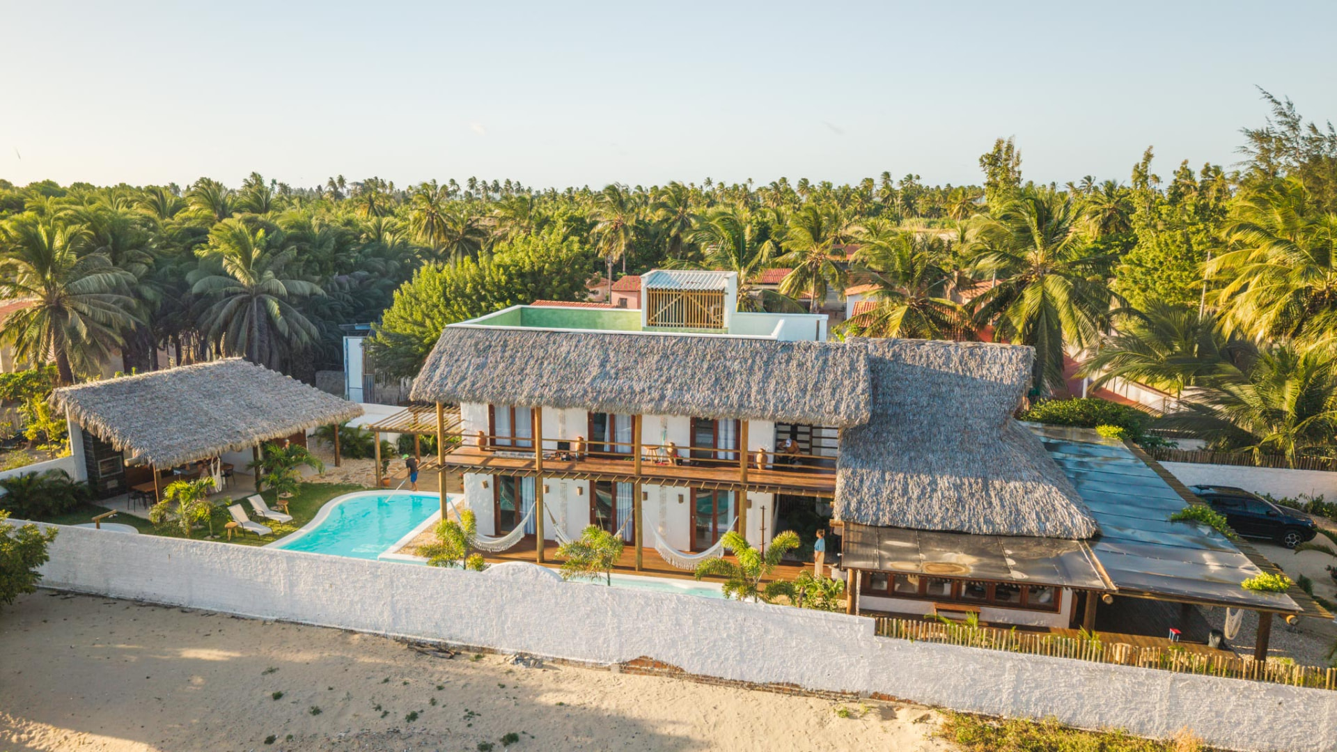 Vista aérea da Azulli Casa Boutique entre coqueiros, com telhado de palha, piscina e varandas